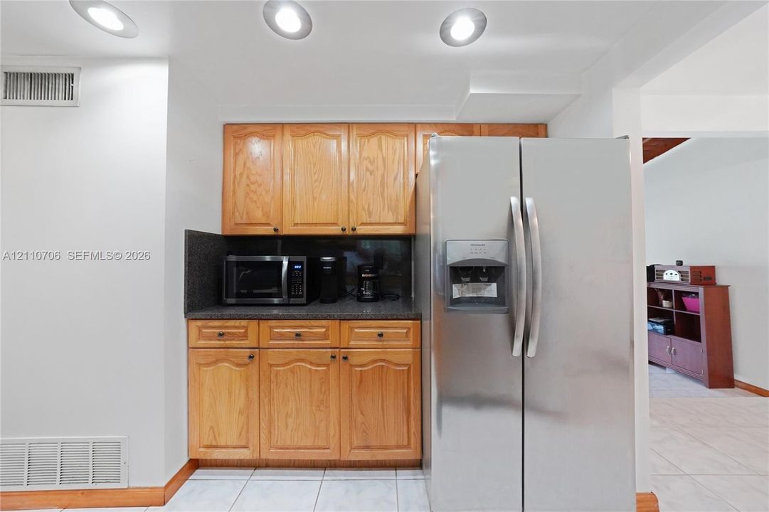 Kitchen area featuring wood cabinetry, stone-finish countertops, stainless steel refrigerator, and recessed ceiling lighting