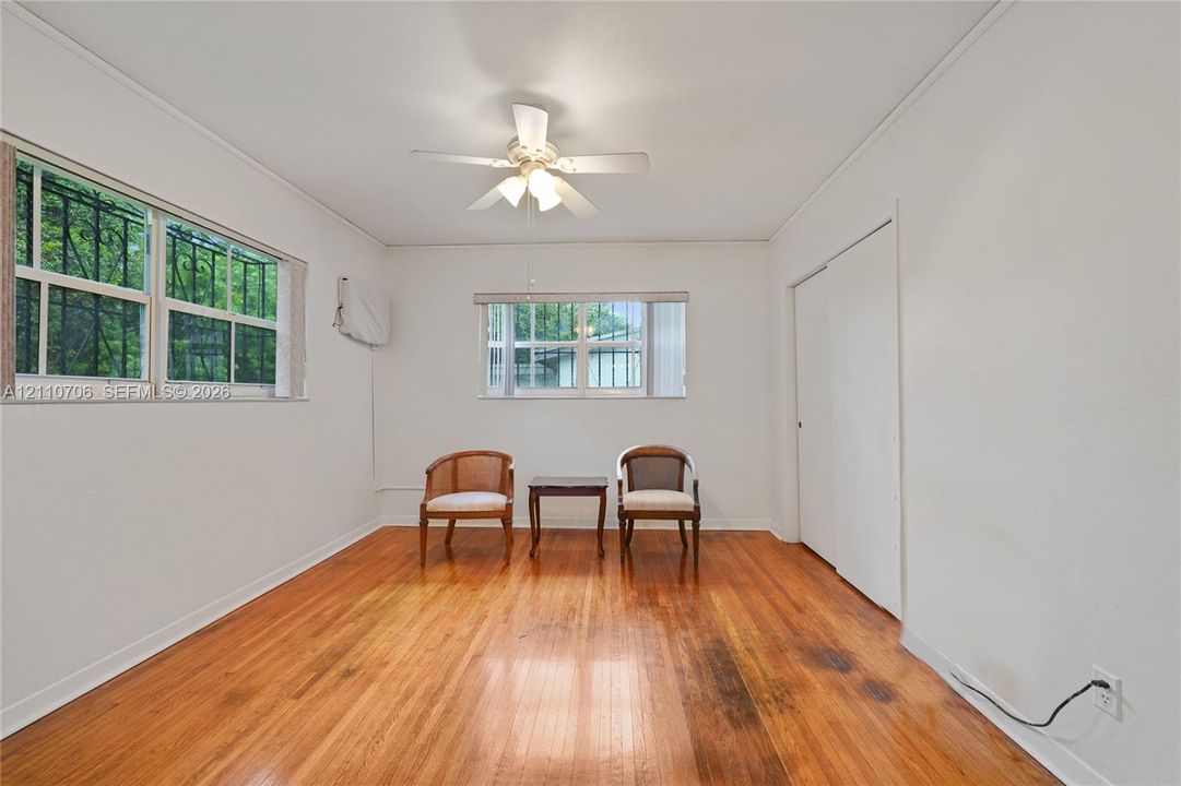 Room interior featuring wood-finish flooring, white walls, a ceiling-mounted fan with integrated lighting, and windows equipped with security bars