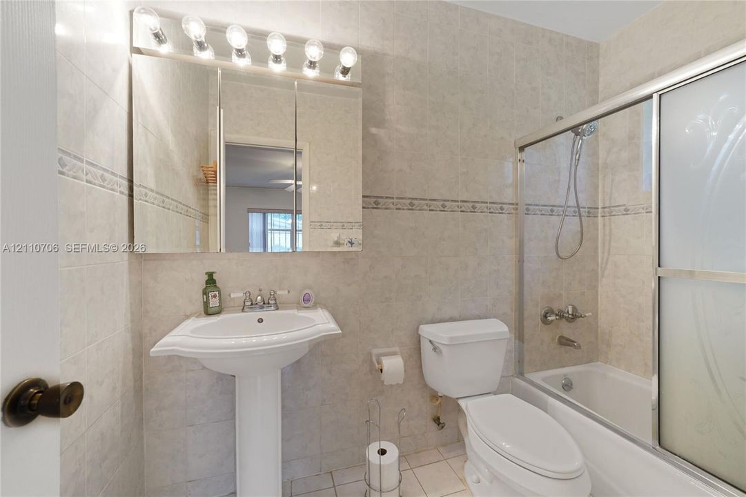 Bathroom featuring full-height wall tiling with decorative inlay, pedestal sink, mirrored medicine cabinet with integrated lighting, and shower-tub combination with sliding glass doors