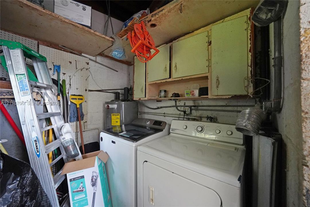 Utility area featuring overhead cabinetry, wall-mounted pegboard, and direct-access plumbing connections