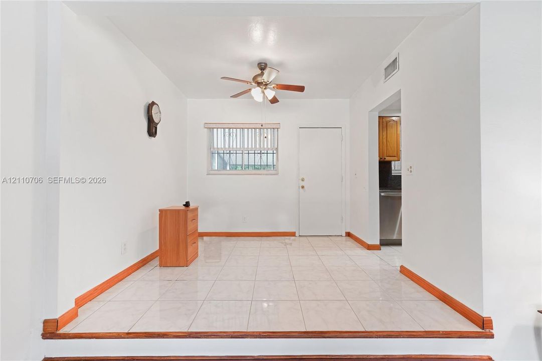 Raised floor area featuring large-format ceramic tile flooring, an elevated wooden threshold, a ceiling fan with integrated lighting, and a window with blinds