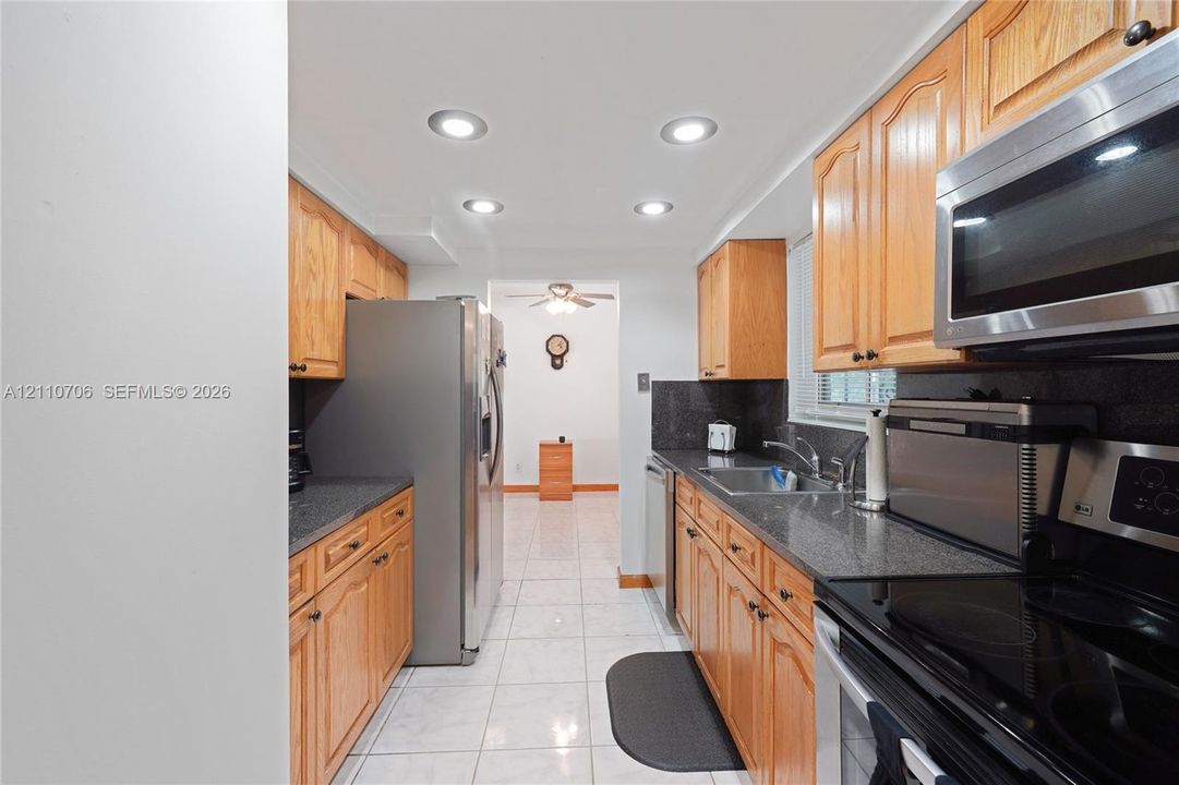 Kitchen featuring wood cabinetry, stone-finish countertops, stainless steel appliances, recessed ceiling lighting, and tile flooring