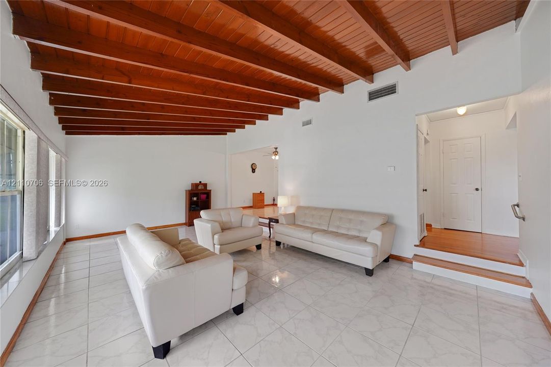 Living area featuring an exposed wood-beam ceiling, large-format tile flooring, and a raised platform with a multi-panel door
