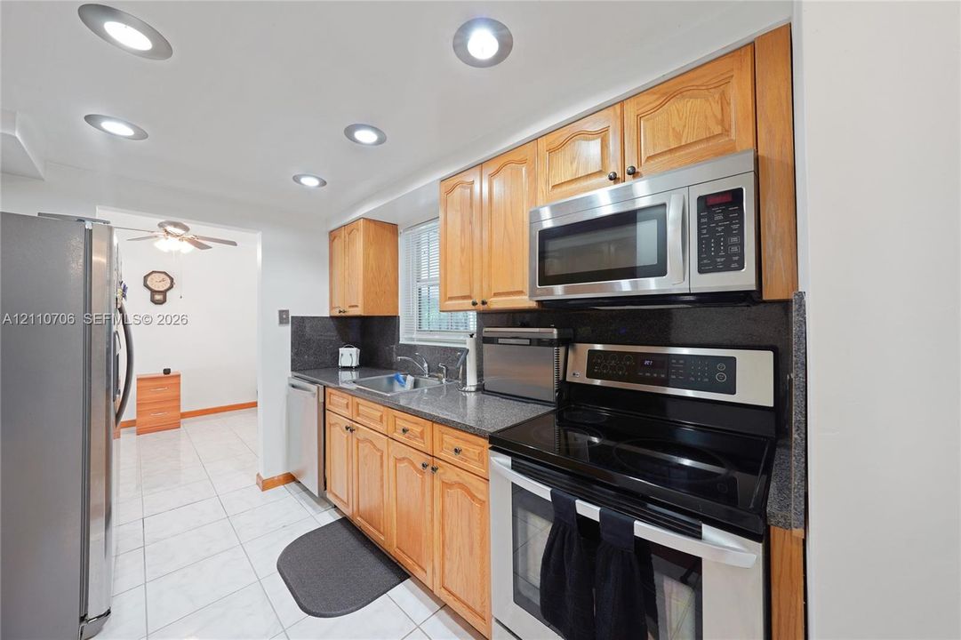 Kitchen featuring wood cabinetry, stone-finish countertops, stainless steel appliances, recessed ceiling lighting, and tile flooring