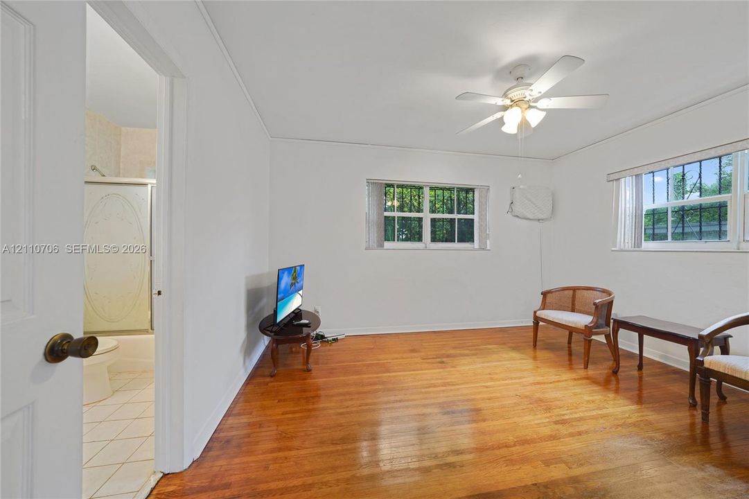Interior space featuring wood-finish flooring, a ceiling fan with integrated lighting, and windows equipped with security bars