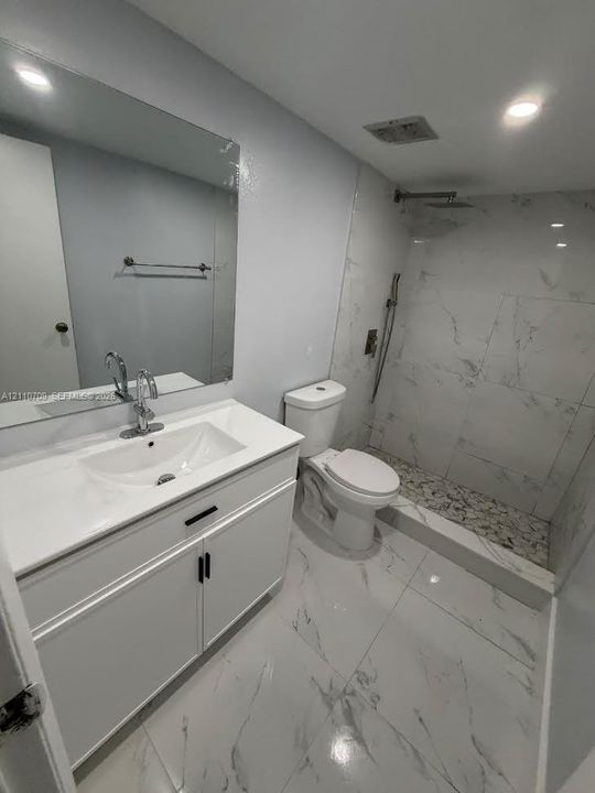 Bathroom featuring a white vanity with a rectangular sink, large-format tile flooring, walk-in shower with stone-tile basin, and wall-to-wall mirror