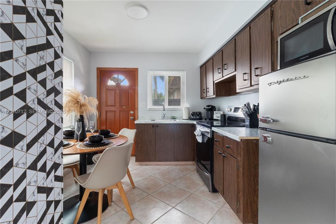 Kitchen featuring dark wood-finish cabinetry, solid-surface countertops, tile flooring, and a decorative geometric accent wall