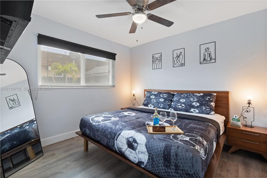 Bedroom featuring wood-finish flooring, a ceiling fan with integrated lighting, and a window with a roller shade