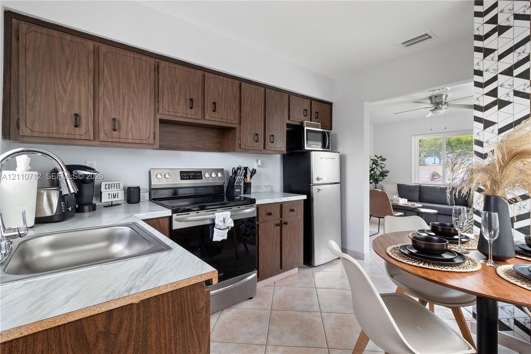 Kitchen featuring dark wood-finish cabinetry, stone-patterned laminate countertops, stainless steel appliances, and ceramic tile flooring