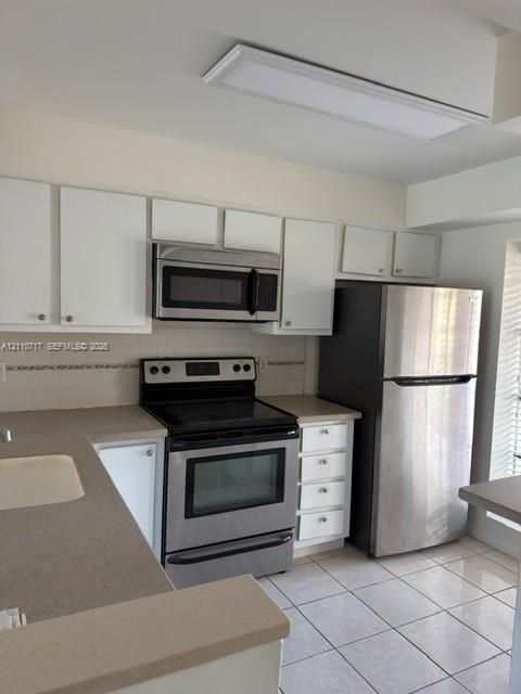 Kitchen featuring white cabinetry, solid-surface countertops, stainless steel appliances, ceramic tile flooring, and a recessed ceiling light fixture
