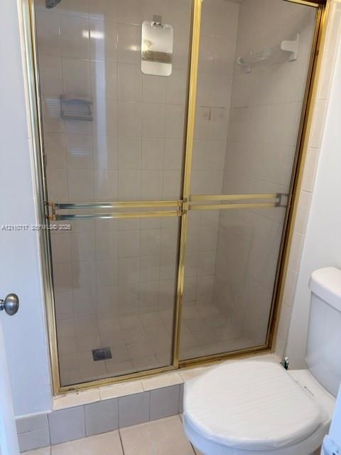 Shower stall featuring sliding glass doors with gold-toned metal framing and interior wall tiling