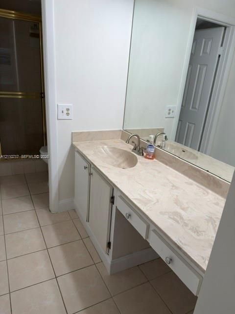 Vanity featuring a light-toned solid surface countertop with an integrated oval sink, full-width wall mirror, lower cabinetry, and ceramic tile flooring