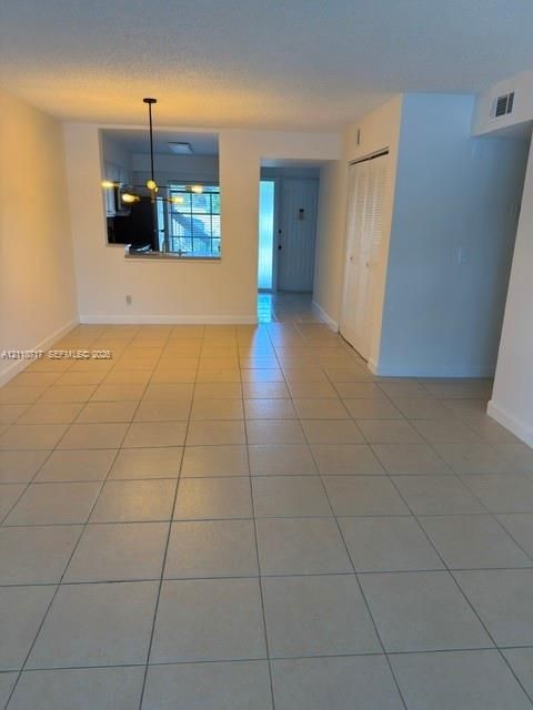 Open-concept area featuring neutral ceramic tile flooring, a multi-arm pendant light fixture, and a pass-through opening
