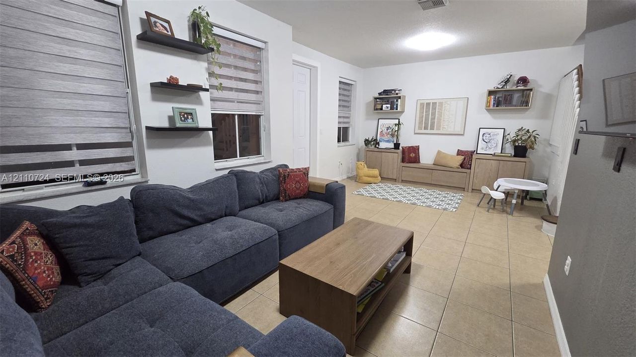 Open-concept interior featuring large-format tile flooring, a staircase with a wooden handrail, and a charcoal accent wall