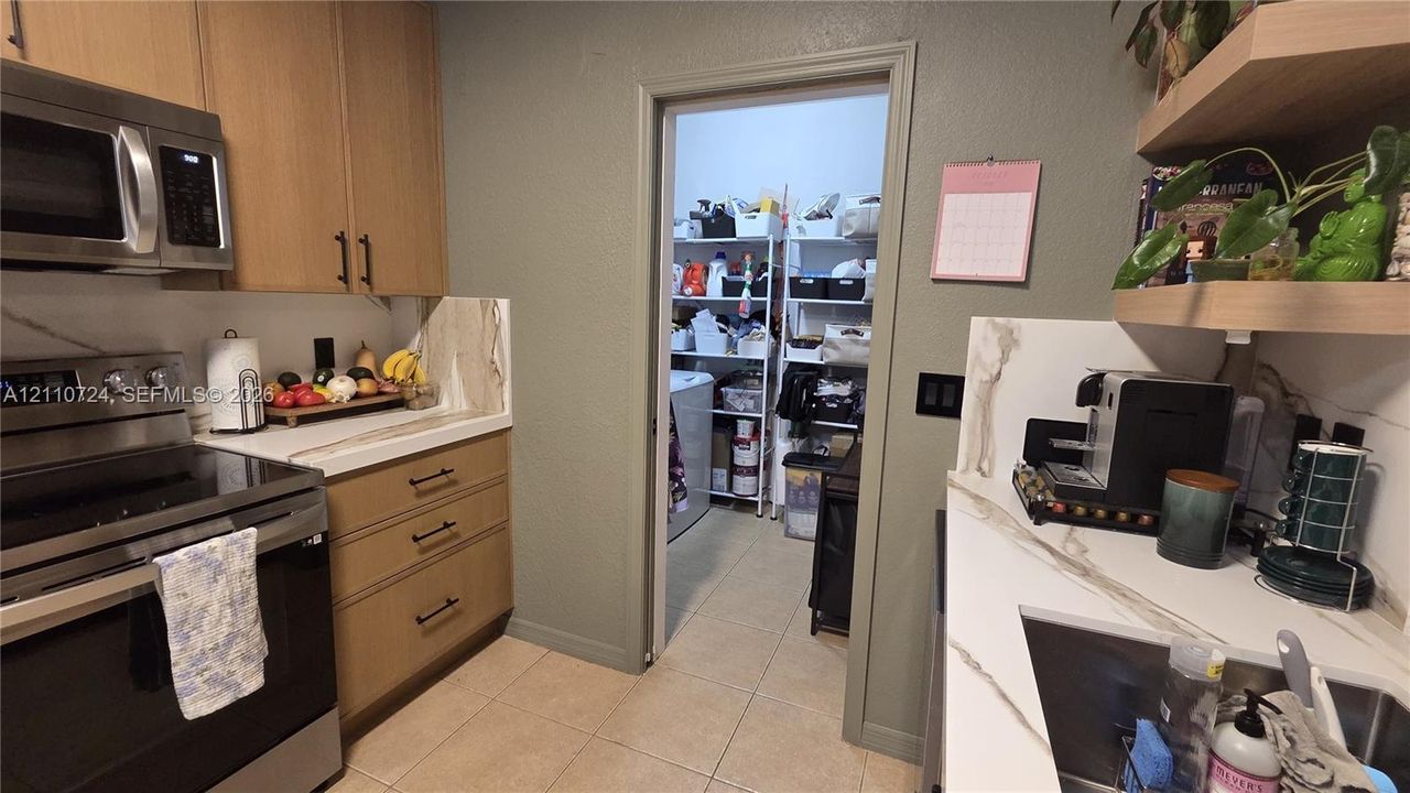 Kitchen featuring flat-panel wood cabinetry, stone-finish countertops with integrated backsplash, stainless steel appliances, and floating wall shelves