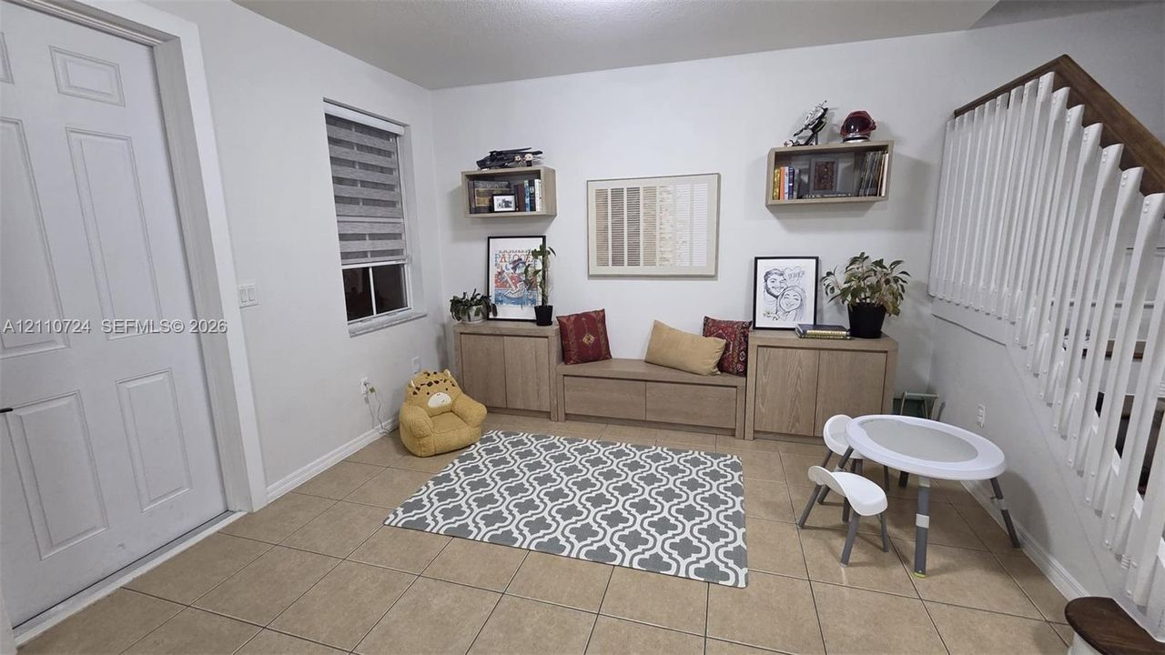 Kitchen featuring flat-panel wood-finish cabinetry, stone-surface countertops with waterfall edge, stainless steel refrigerator, undermount sink with arched pull-down faucet, and neutral tile flooring