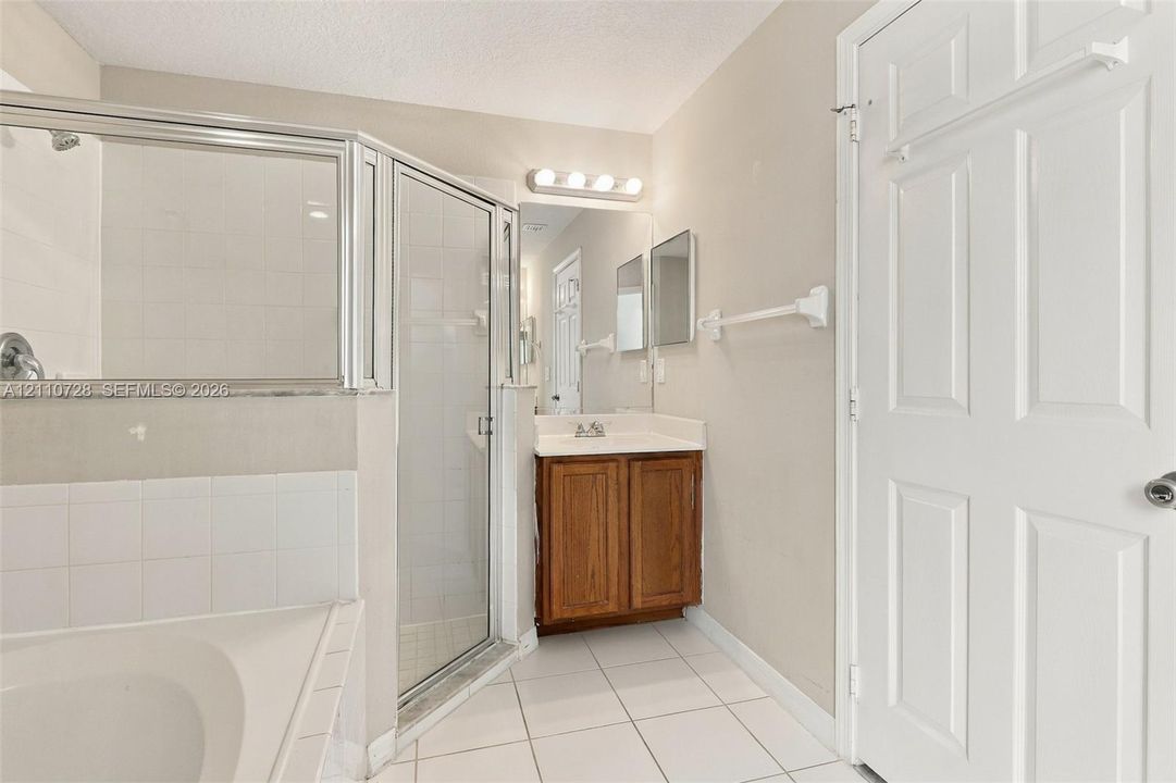 Bathroom featuring a corner soaking tub, glass-enclosed shower, wood-finish vanity, and tiled flooring