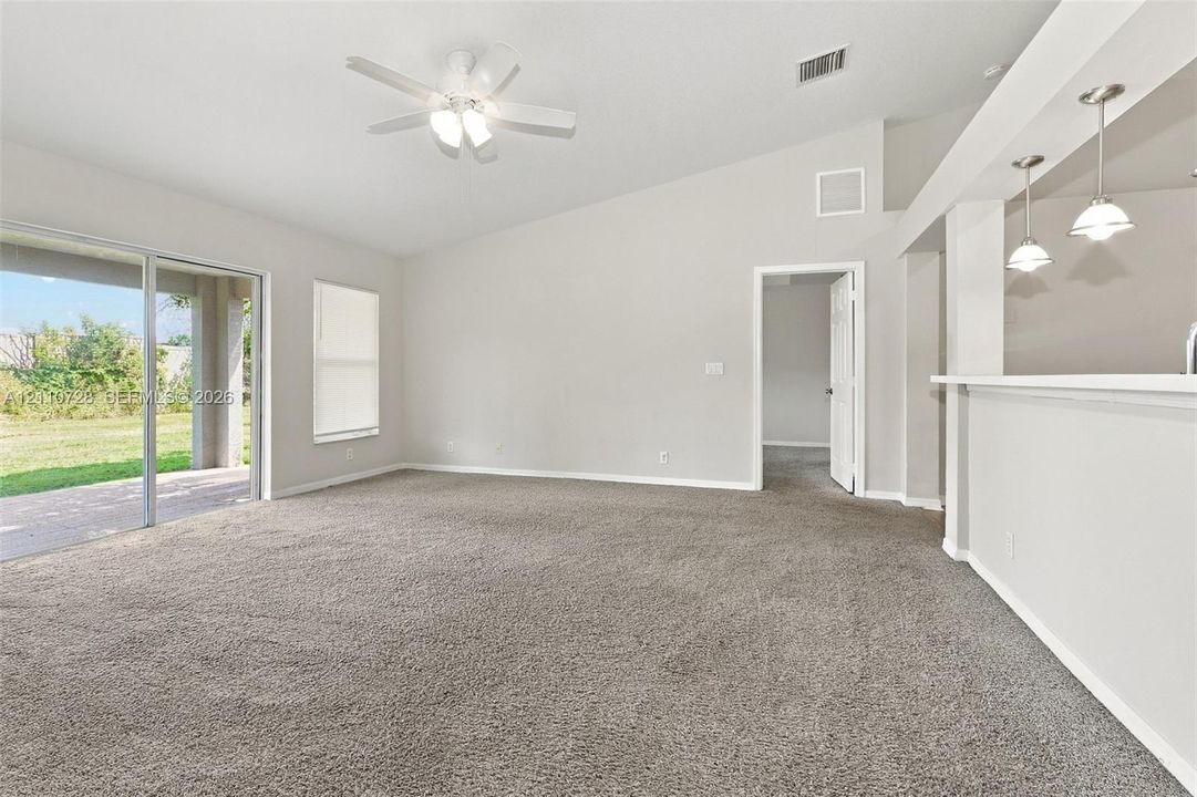 Vaulted ceilings featuring a central ceiling fan, neutral carpeting, sliding glass doors, and a kitchen pass-through counter with dual pendant lighting