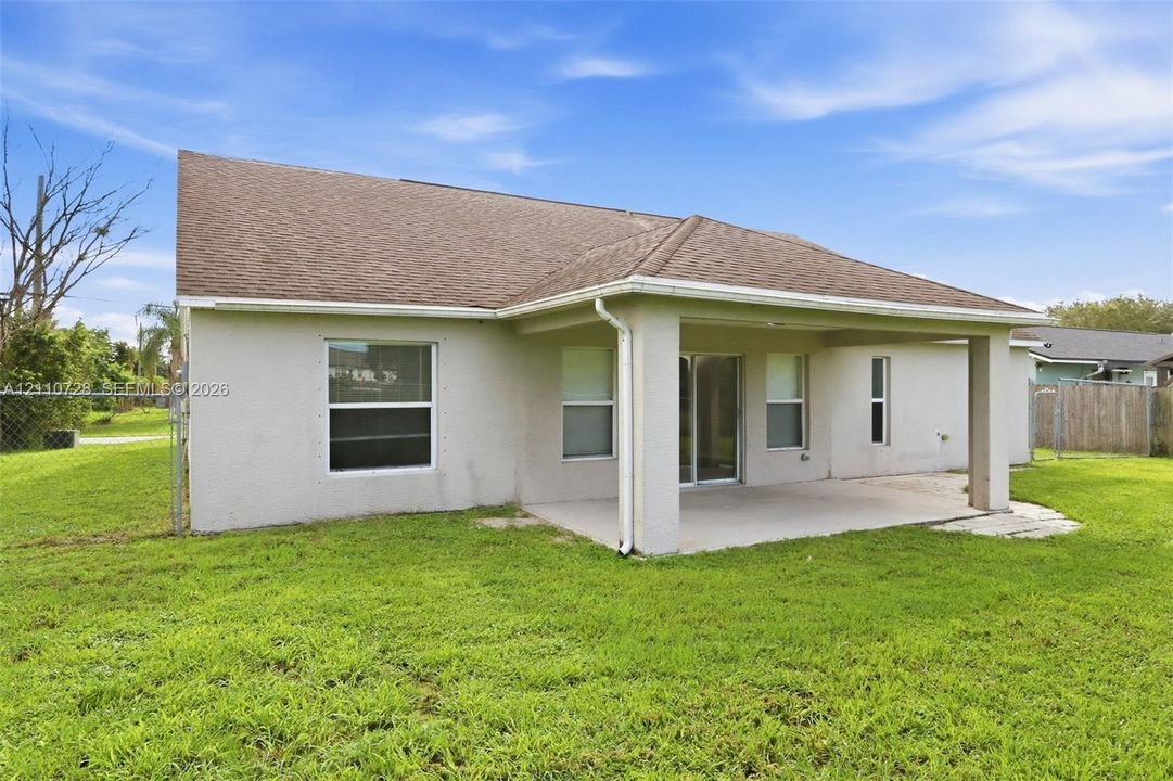 Rear exterior featuring a covered concrete patio, light-colored stucco siding, a hip roof, sliding glass doors, and a fenced backyard