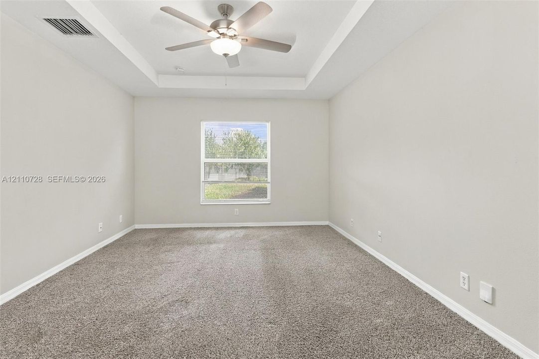 Neutral-toned room featuring a tray ceiling, carpeted flooring, and a central ceiling fan with an integrated light fixture