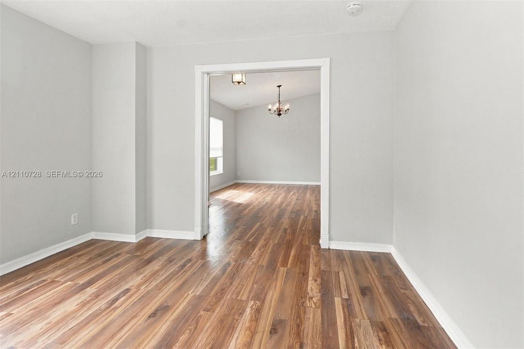 Neutral-toned walls paired with wood-finish flooring throughout, featuring a cased interior opening and a multi-arm ceiling chandelier