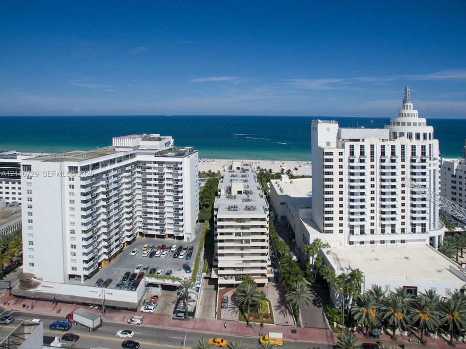 Aerial perspective of high-rise structures situated along the coastline, featuring beachfront access, multiple tiered balconies, and paved surface parking