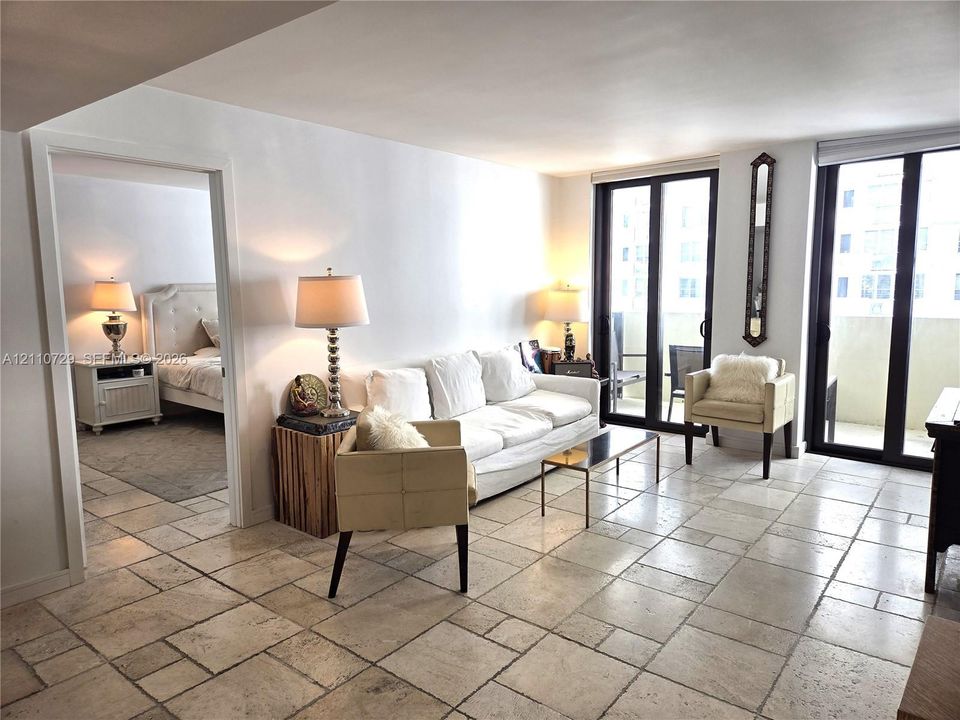 Natural stone tile flooring throughout the living area, floor-to-ceiling glass sliding doors, and private exterior balcony access