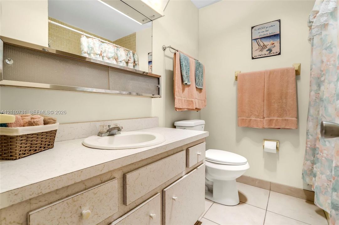 Bathroom featuring a solid-surface vanity countertop with an integrated basin, metal-framed mirrored cabinetry, and ceramic tile flooring