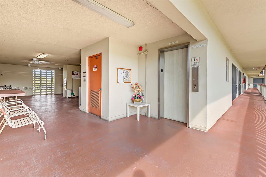 Covered exterior corridor featuring a dedicated elevator, recessed ceiling lighting, and a painted concrete surface