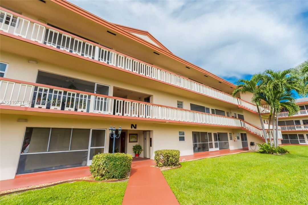 Multi-story residential exterior featuring screened balconies, white railings, stucco facade, and manicured landscaping