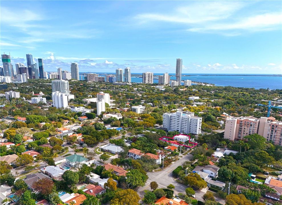 Aerial perspective showcasing the property location within a dense urban landscape featuring a skyline, coastal water, and mature tree canopy
