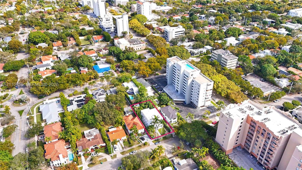 Aerial perspective of a multi-story residential building featuring a flat roofline, white exterior facade, and mature palm trees located within a densely treed urban environment