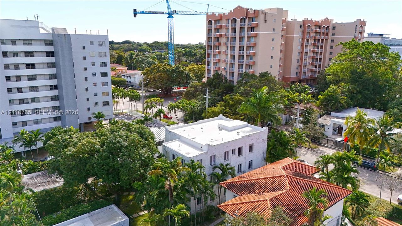 Aerial perspective of urban landscape featuring multi-story residential architecture, terracotta roof tiling, white exterior facades, and dense mature palm and hardwood foliage