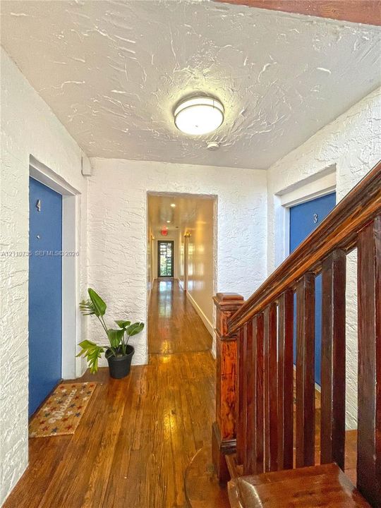 Hallway featuring wood-finish flooring, textured white walls, a flush-mount ceiling light, and a wooden staircase railing