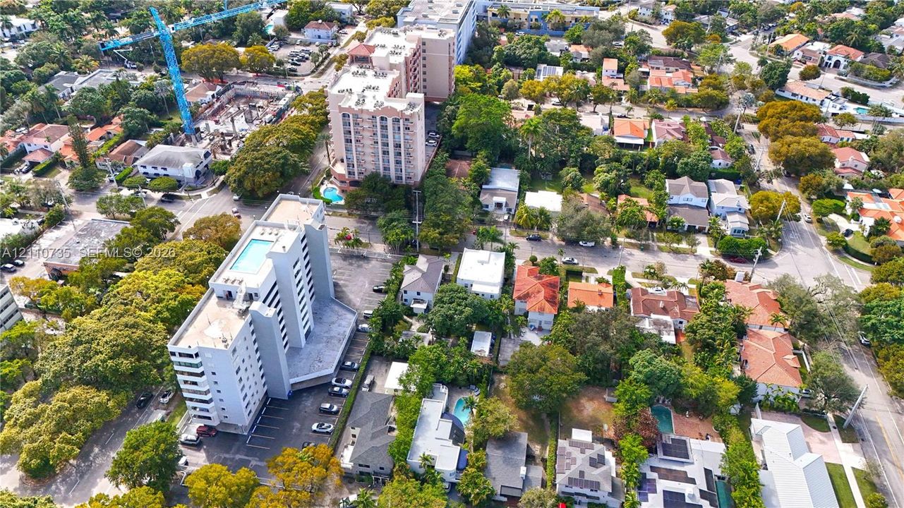 Aerial perspective of a dense urban neighborhood featuring mature tree canopies, residential streets, and multi-story condominium buildings