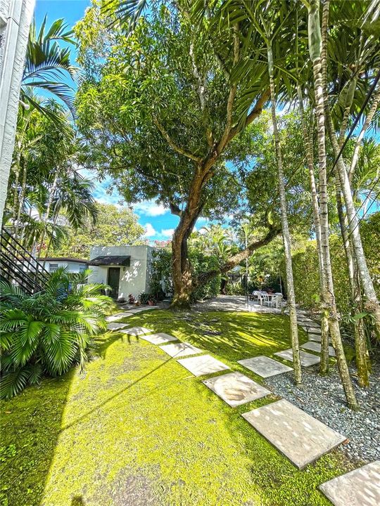 Outdoor space featuring a lawn, mature trees, stone paver pathway, and gravel ground cover