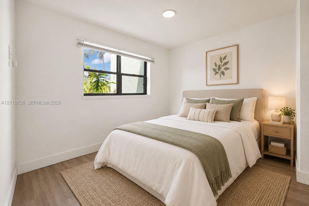 Neutral wall paint, wood-finish flooring, and a window with a black frame featuring exterior landscape visibility