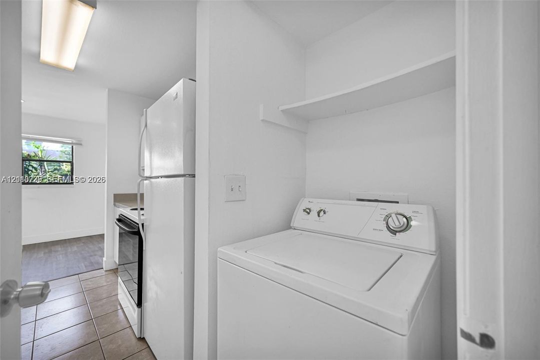 Laundry closet featuring overhead shelving, tile flooring, and integrated white appliances including a top-load washer, refrigerator, and oven range