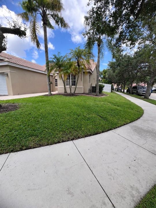Single-story exterior featuring light-toned stucco siding, a tiled roof, mature palm trees, and a manicured lawn