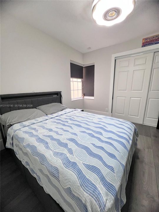 Room interior featuring wood-finish flooring, a double-door closet with paneled detailing, a multi-pane window, and a circular flush-mount ceiling fixture