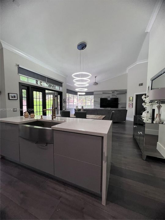 Kitchen island with stone-finish countertop, stainless steel farmhouse sink, multi-tiered ring pendant light, and dark-finish wood-finish flooring