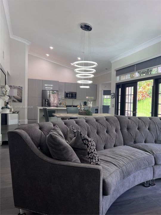 Open-concept interior featuring vaulted ceilings, modern multi-tier LED ring chandelier, dark wood-finish flooring, and floor-to-ceiling multi-panel glass doors
