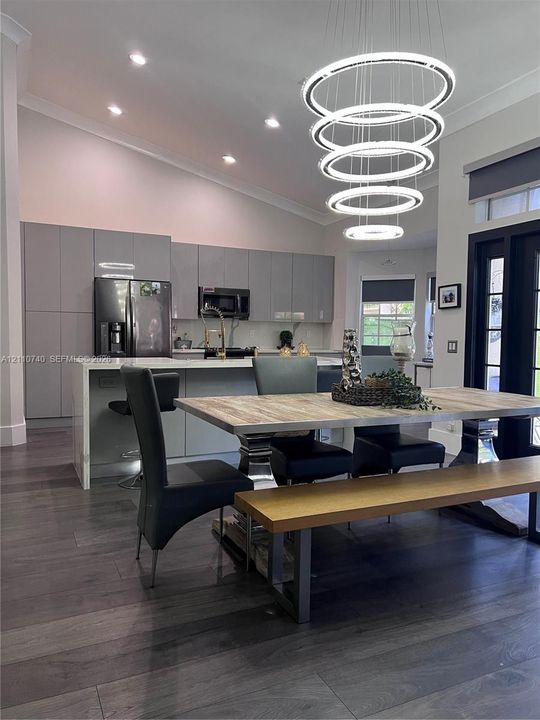 Kitchen featuring full-height flat-panel cabinetry, a stone-topped waterfall edge island, recessed ceiling lighting, a multi-tiered circular pendant fixture, and wood-finish flooring