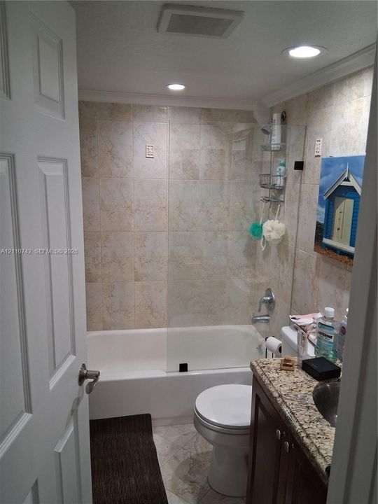 Full bathroom featuring a shower-tub combination with glass panel enclosure, tile-surround walls, stone-finish countertop, and recessed ceiling lighting