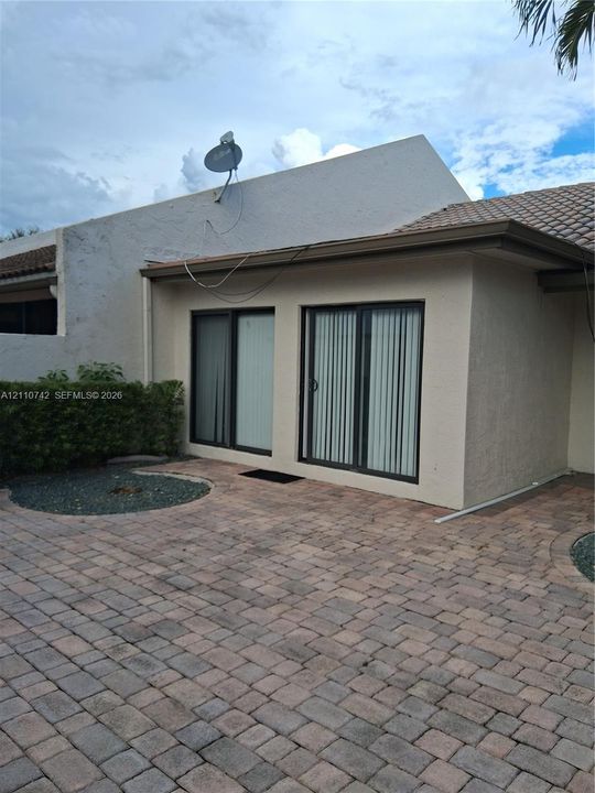 Exterior patio featuring stone paver flooring, stucco wall finish, tiled roofing, and dual sliding glass doors
