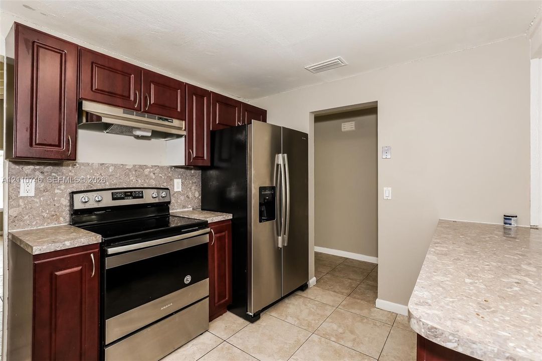 Kitchen featuring deep-toned cabinetry, stone-patterned countertops, a stainless steel range, a stainless steel refrigerator, and tiled flooring
