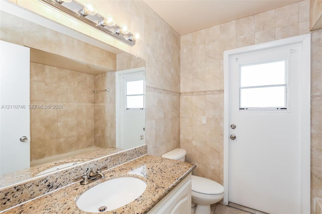 Stone-finish countertop with an integrated basin, wall-to-wall mirror, tiled wall surfaces, and light-tone cabinetry