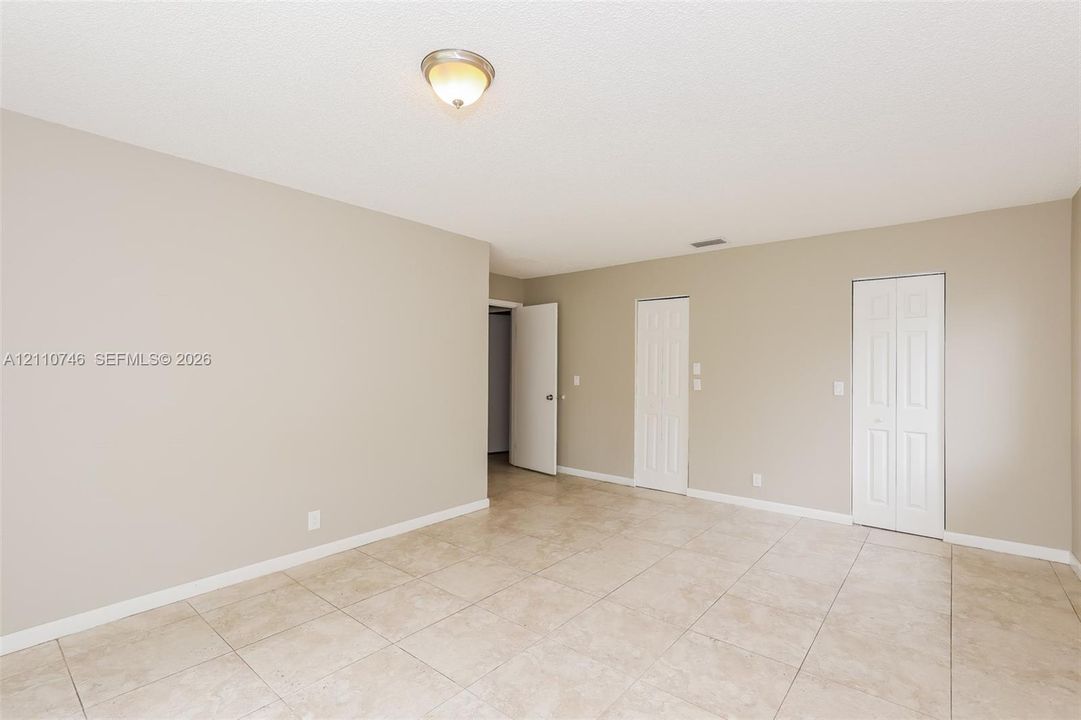 Neutral-toned interior featuring large-format tile flooring, textured ceiling finish, two bi-fold closet doors, and a central dome-style ceiling light fixture