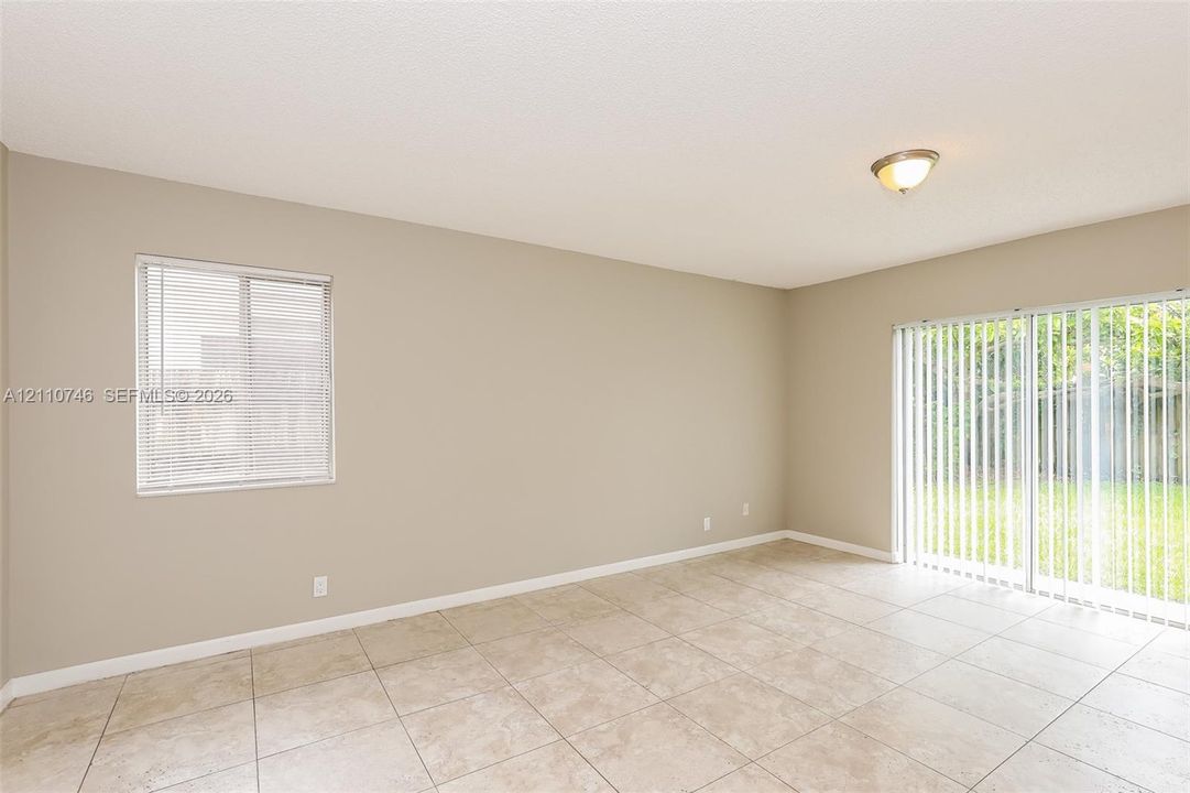 Neutral-toned interior space featuring light-colored tile flooring, a single-hung window with blinds, and sliding glass doors