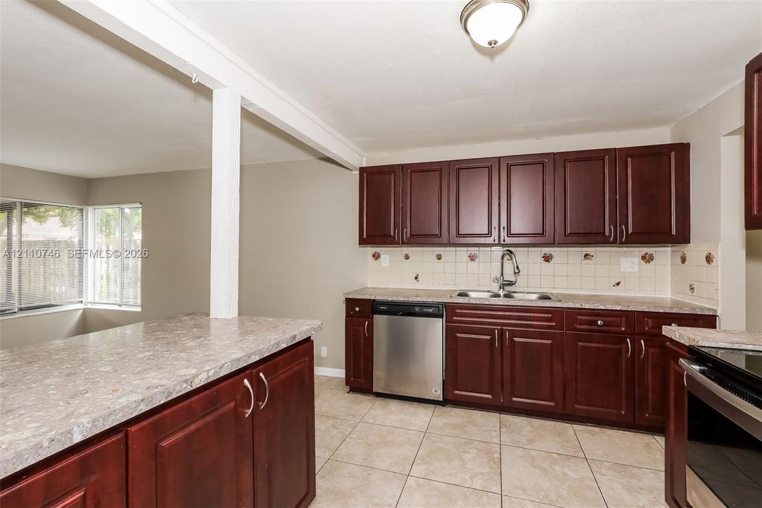 Kitchen featuring dark-finish cabinetry, stone-texture laminate countertops, stainless steel dishwasher, tile backsplash, and ceramic tile flooring